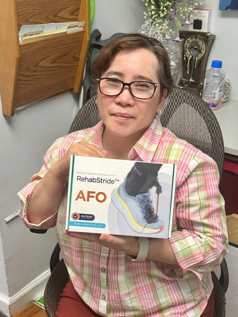 Woman smiling and holding a RehabStride AFO brace box inside an office setting